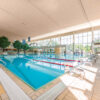 Hallenbad mit großem Schwimmbecken und Fensterfront.