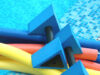 Bunte Schwimmnudeln und Trainingsgeräte auf Fliesen am Beckenrand.