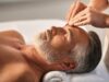 Mann liegt entspannt auf einer Massageliege und wird an der Stirn massiert.