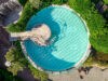 Draufsicht auf ein rundes Schwimmbecken mit Treppe und umliegender Begrünung, Liegestühlen und Gartenwegen.